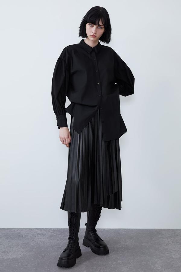 Camisa de popelín amplia con la manga larga abullonada y bajo asimétrico (Zara, 22,95 euros) Falda confeccionada en un tejido efecto piel plisado, de tiro alto y bajo asimétrico. Lleva un cierre lateral con hebilla y botón oculto (Zara, 29,95 euros). Bota plana de piel de color negro con cordones, punta cuadrada y tirador trasero (Zara, 99,95 euros). La suela es gruesa tipo track y cierra con una cremallera interior.