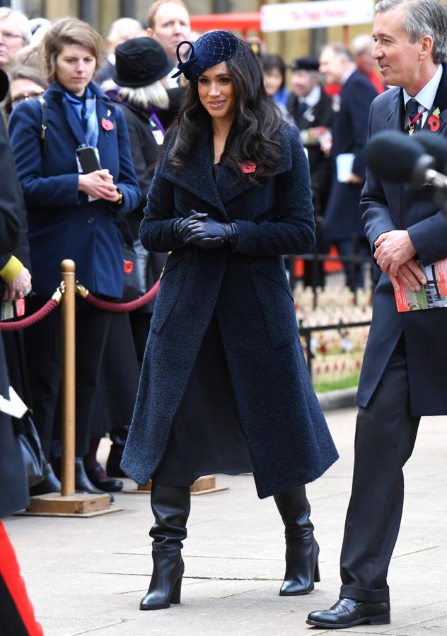 Meghan Markle ha combinado su abrigo azul marino de Sentaler con un vestido de satén 'navy blue', unas botas altas negras de Tamara Mellon y un elegante tocado de inspiración retro de Philip Treacy.