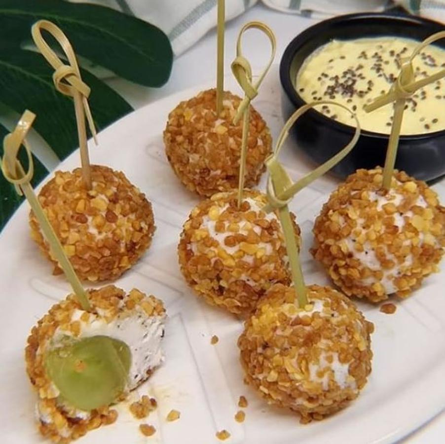 Ingredientes:-Uvas (también serviría arándanos, gajos de mandarina o frambuesas)-Queso de cabra-Trufa (o especias al gusto)-Almendra picada (u otro fruto seco o semillas)Preparación:Se lavan las uvas y se reservan.Se mezcla el queso de cabra con la trufa y se envuelve cada uva haciendo bolitas.Se pasan las bolitas por el fruto seco picado, se pincha con un palillo, y listo.Se puede acompañar con una salsa de mango al jengibre, batiendo mango, jengibre y queso fresco batido.