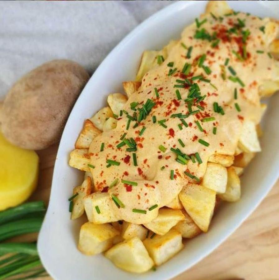 Ingredientes:-Patatas-2 puñados de anacardos (remojo 8 horas)-2 dientes de ajo-1 cebolla tierna-1 puerro-1 cdta pimentón dulce o picante-Sal-AOVE-2 vasos de caldo vegetalPreparación:Las patatas las pelamos, cortamos y lavamos para quitarle todo el almidón. Después las deje media hora en agua fría con hielo.Se escurre bien, se las seca y se salpimentan con aove y sal, las ponemos en una bandeja sobre papel vegetal separaditas (ahí el truco para que salgan crujientes) y las llevamos al horno a 200°C unos 20-25 minutos hasta que estén doraditas.Pocharemos los vegetales en aove cortados muy finitos.Una vez pochados los trituramos con los anacardos enjuagados y escurridos junto al caldo vegetal hasta formar una pasta bastante fina.Calentar aove en una sartén hasta que comience a hervir retíralo del fuego (esto es importante ya que el pimentón se arrebata y puede amargar) y añádele una cucharadita de pimentón mezclar bien que se emulsionen y el pimentón se integre con el aceite.Después echamos la salsa de anacardos mezclamos bien y volvemos a llevar a fuego hasta que comience a hervir apagamos y servimos junto con las patatas.