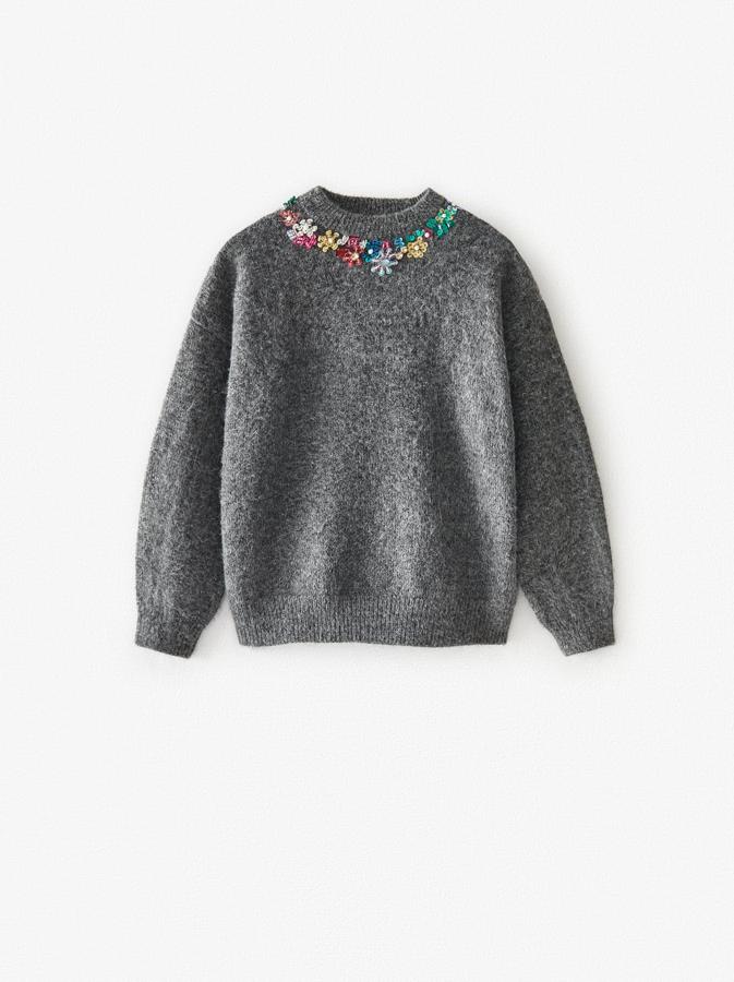 Jersey gris de cuello perkins con apliques de lentejuelas en forma de flor. Costaba 25,95 euros y está rebajada a 15,99 euros.