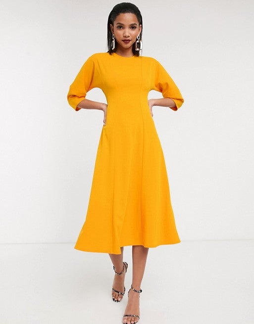 Este  vestido minimalista de corte midi  con costuras en tono mostaza da la oportunidad de jugar con los complementos para quienes prefieran no dar todo el protagonismo a la prenda y equilibrar su look. (44,99 euros).