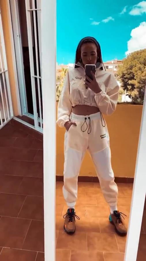 Chándal de Bershka combinado en blanco y rosa con sudadera cropped con bajo fruncido y pantalones jogger. Lo conjunta con zapatillas de Reebok.