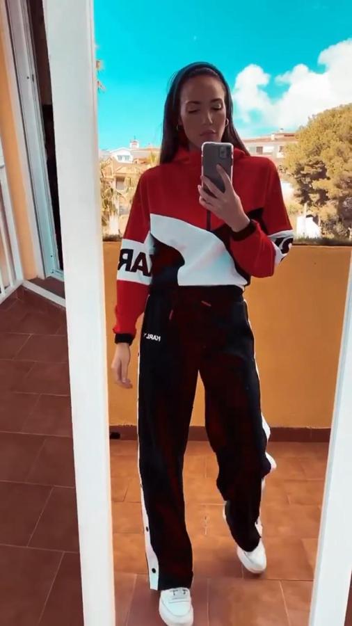 Conjunto deportivo de Karl Lagerfeld con pantalón ancho con botones en los laterales y sudadera con cremallera en rojo, blanco y negro. Lo ha combinado con zapatillas blancas de Reebok.