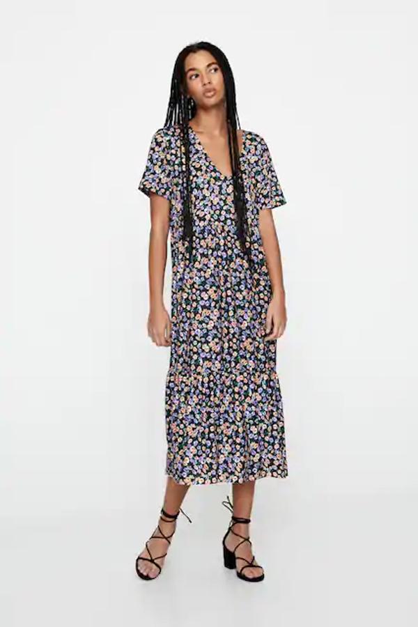 Con fondo negro y estampado de flores a contraste lilas y naranja, este vestido de Pull&Bear está confeccionado en tejido de bámbula y tiene las mangas cortas. Con escote de pico y diseño midi, cuesta 19,99 euros y está disponible entre las tallas XS y XL.
