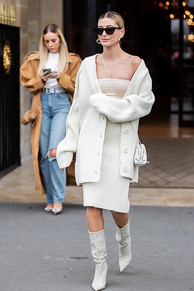 Hailey Bieber lleva un look monocromático en beis con un conjunto de punto, microtop color carne y botas a juego.