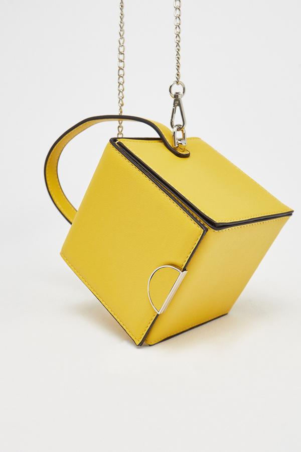 En color amarillo (también disponible en color naranja), este bolso en forma de cubo con cierre de imán, tiene un asa larga de cadena. Tiene un precio de 11,85 euros.