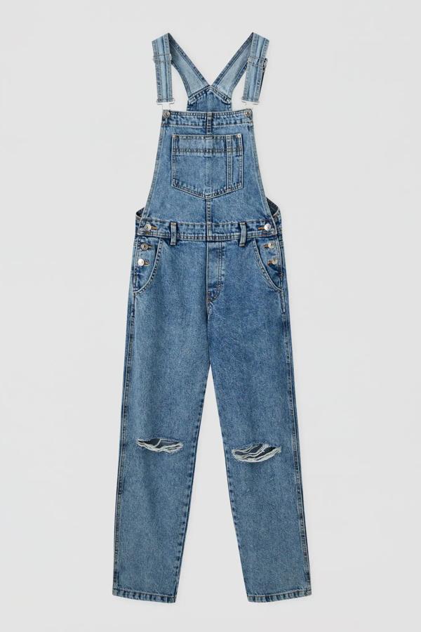 Este peto vaquero largo con rotos en la rodilla es de Pull & Bear y tiene un precio de 29,99 euros. Con tirantes ajustables, cuenta con bolsillos y cintura con trabillas.
