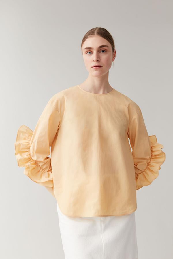 Blusa amarilla de popelín con volantes en las mangas, de Cos (69 euros).