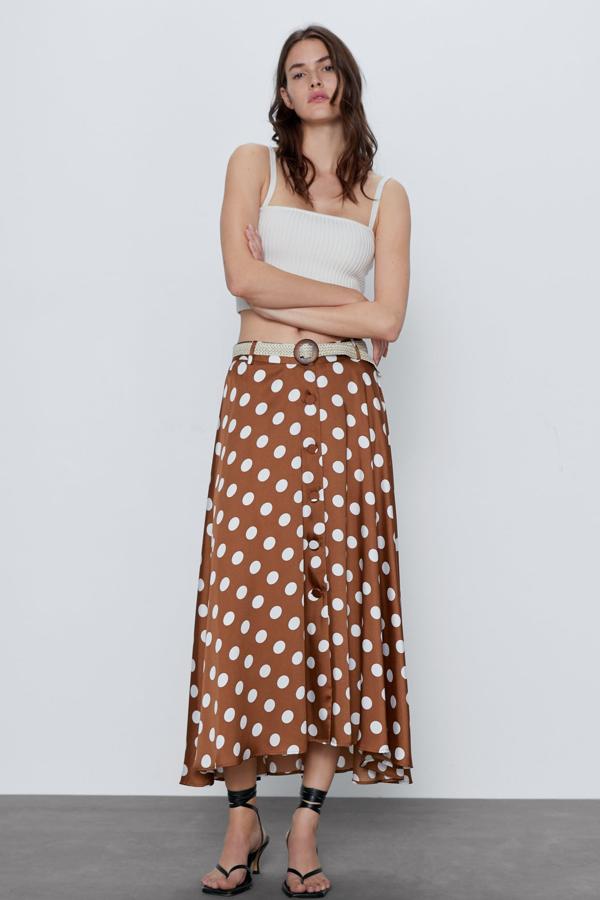 En color marrón con lunares en crudo, esta falda midi de tiro alto con cinturón es de Zara. Con bajo asimétrico y cierre frontal con botones forrados, tiene un precio de 29,95 euros.