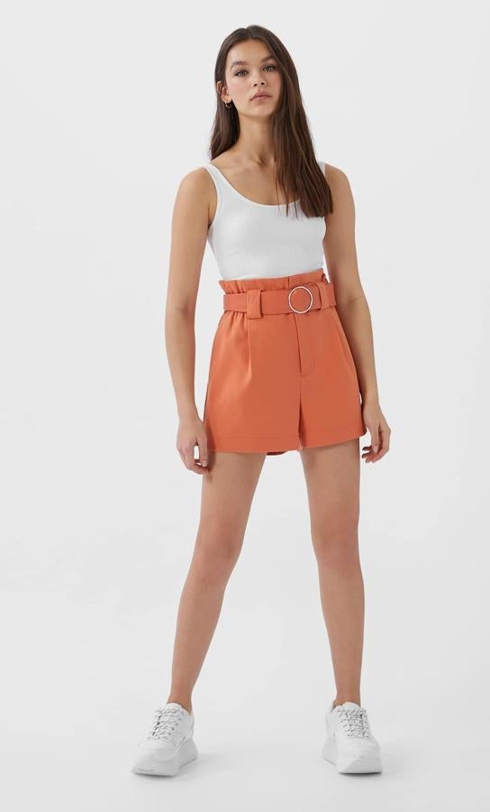 Este pantalón corto de pinzas en color coral con cinturón con hebilla metálica redonda es de Stradivarius y tiene un precio de 17,99 euros.