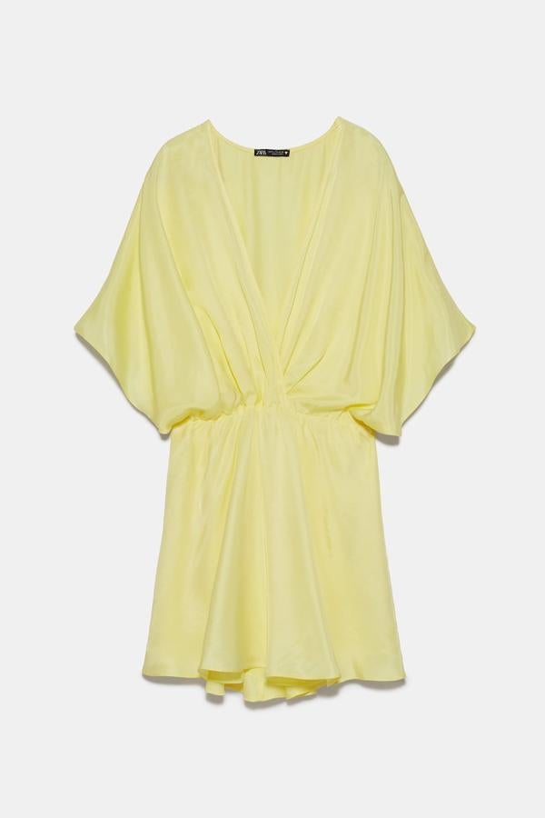 Vestido corto satinado en color amarillo con escote de pico cruzado y manga corta amplia. Tiene un precio de 29,95 euros.