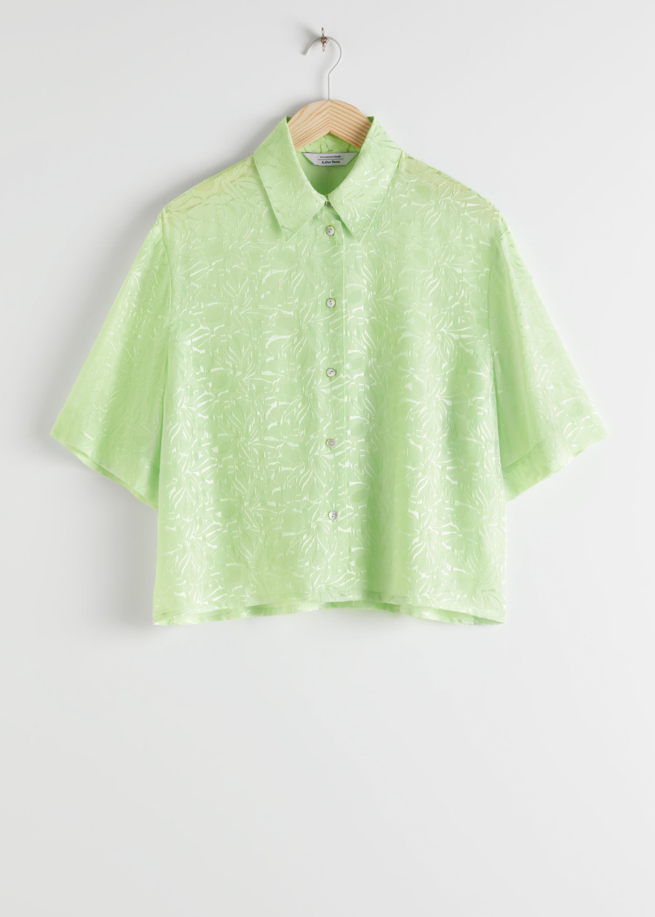 Esta blusa con estampado jacquard y tejido satinado es un flechazo, por su color verde, su tejido fluido y su corte cropped para lucir los pantalones blancos a la perfección de arriba a abajo. (69 euros).