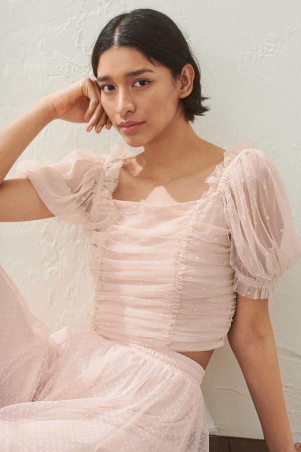 Confeccionado en malla estampada, con mangas cortas abullonadas y elástico con volante en los hombros y los puños, este cuerpo de H&M en rosa empolvado viene con forro y pliegues drapeados delante y detrás y fruncido ancho en la espalda. Cuesta 19,99 euros y está disponible entre las tallas 38 y 50.