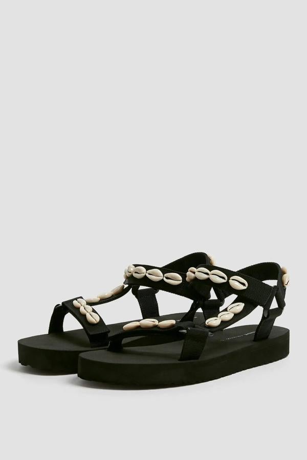 Sandalia plana de estilo deportivo en color negro con detalle de conchas. La suela tiene una altura de 2,5 centímetros y un precio de 29,99 euros.