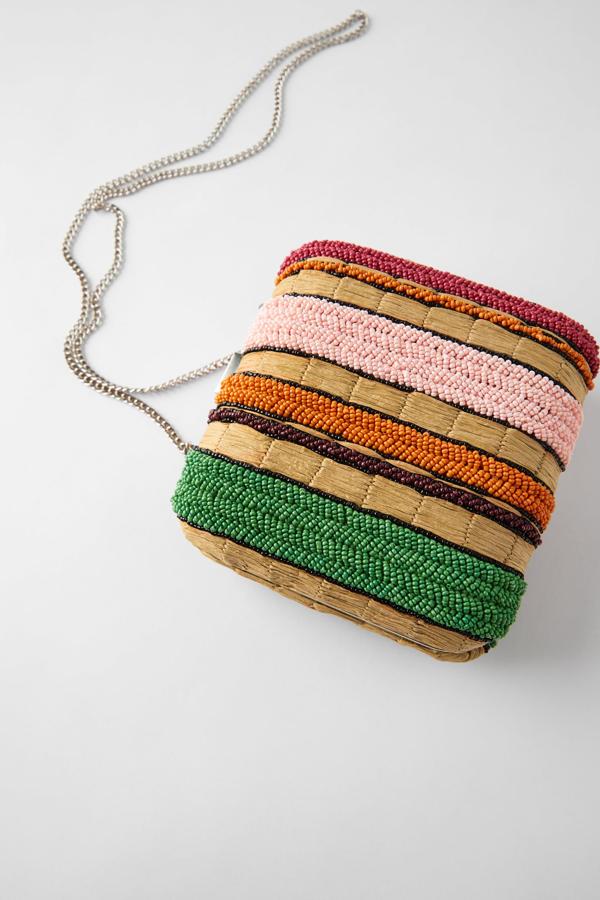 Este bolso bandolera formato caja cuenta con cuerpo con detalle de papel natural y abalorios de diferentes colores dispuestos en franjas. Con asa de hombro con cadena, tiene un precio de 35,95 euros.