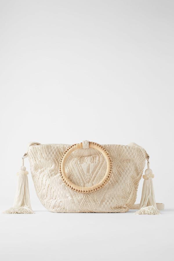 Este bolso en formato saca en color blanco cuenta con cuerpo de tejido jaspeado con cuentas y detalle de maxi borlas con abalorios. Tiene un precio de 39,95 euros y dispone de asas de mano circulares de bambú.