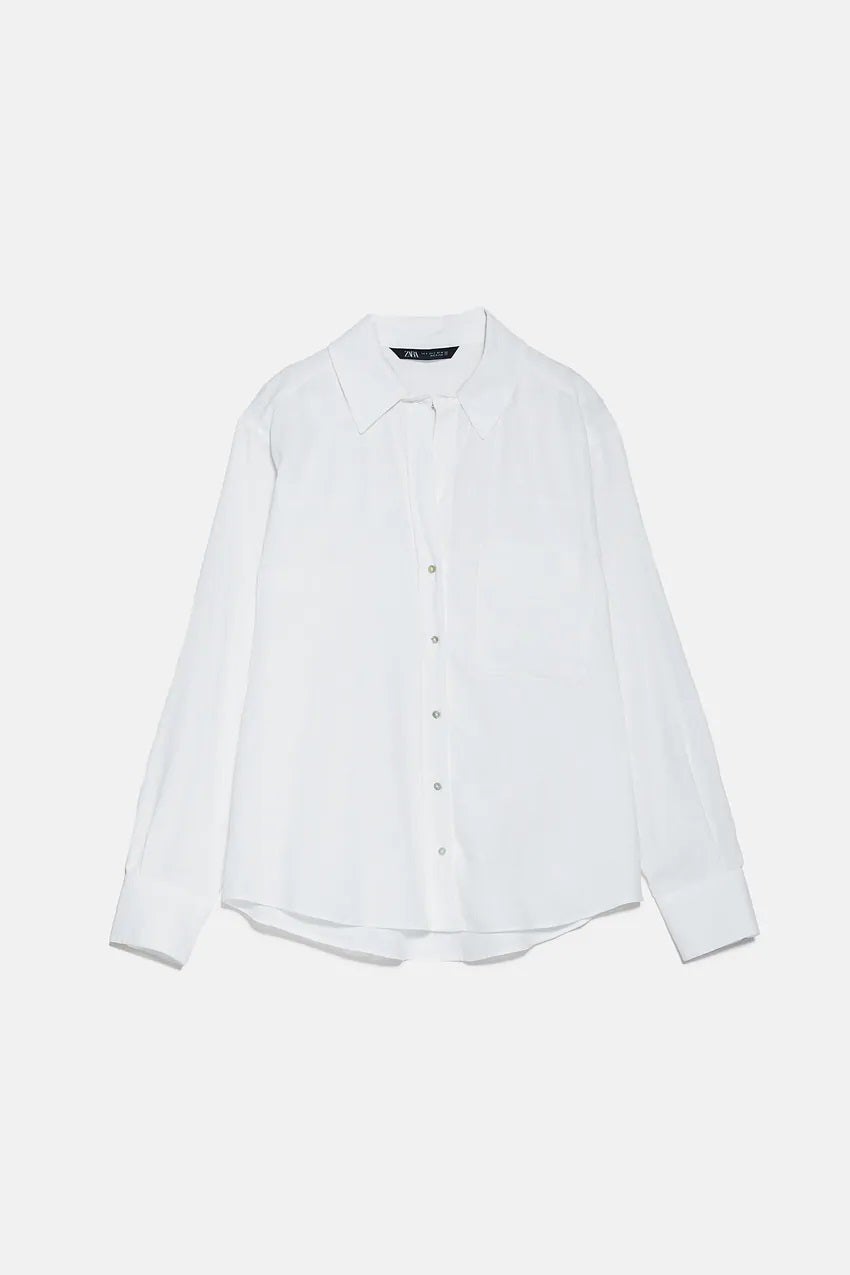Camisa blanca con cierre de botones, maga larga y tejido de lino. De Zara. (22,95 euros). Perfecta para cualquier ocasión.