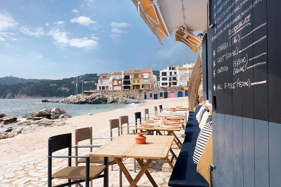 Tarruella Trenchs Studio, dirigido por la laureada interiorista Sandra Tarruella, se encargó de renovar este icono gastronómico sobre la misma arena de Calella de Palafrugell por su 25 aniversario. Arroces y mariscos, espejos que multiplican las vistas al mar desde el salón y materiales como el mimbre de las lámparas y la madera (azul en las ventanas y blanca dentro). Más marinero, imposible.