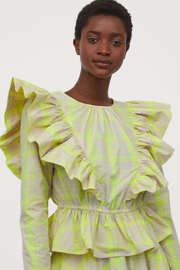 Blusa de tela con cuello redondo y cierre de lágrima con botón en la nuca. Lleva la manga larga con volantes anchos delante, costura elástica fina en la cintura y peplo y va sin forrar (34,99 euros). va a juego de una falda corta con vuelo y bolsillos al bies discretos (39,99 euros).