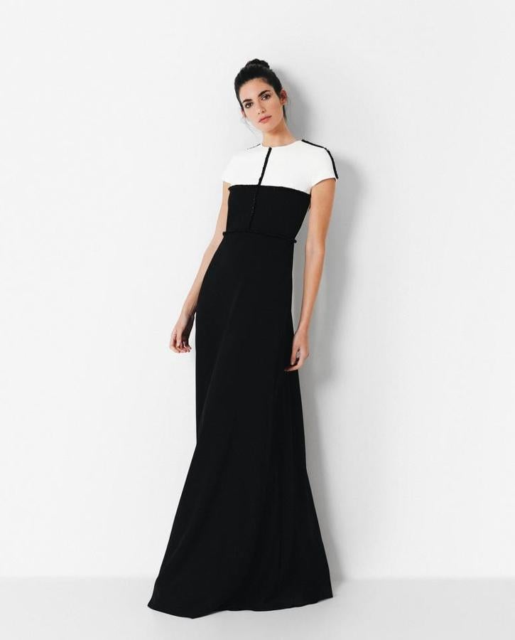 Vestido de invitada largo bicolor negro y blanco de crepé con cuello a la caja y manga corta. Tira de piedra que recorre el cuerpo de forma vertical y horizontal bordadas a mano sobre el vestido. Corte en la cintura con falda recta y su gran protagonista, su espalda abierta y gran lazada negra. Un vestido muy especial para ocasiones igual de especiales. Pasa de 395 euros a 276 euros.