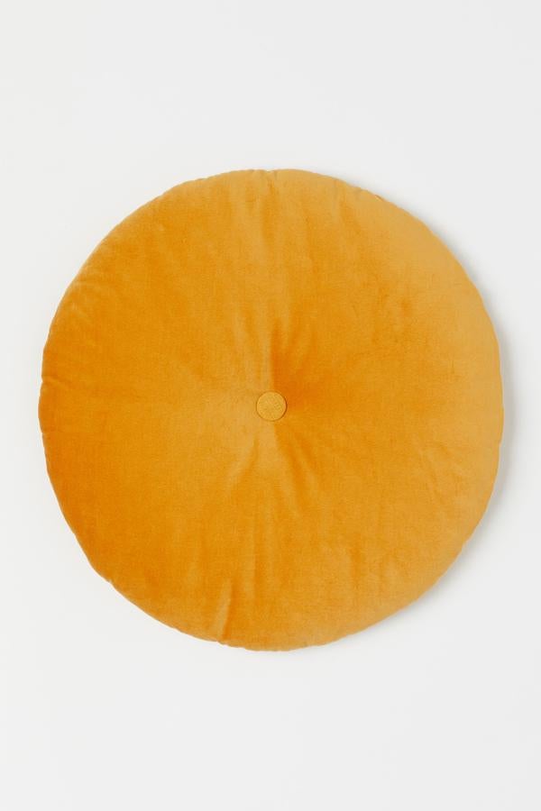 En color amarillo, este cojín redondo con parte superior de terciopelo y trasera de algodón tiene un diámetro de 42 centímetros y un precio de 8,99 euros.