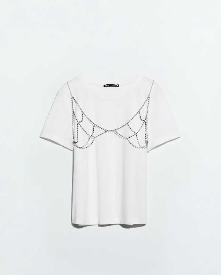Camiseta de cuello redondo y manga corta, con una aplicación metálica con joyas en el delantero (Zara, 19,95 euros).