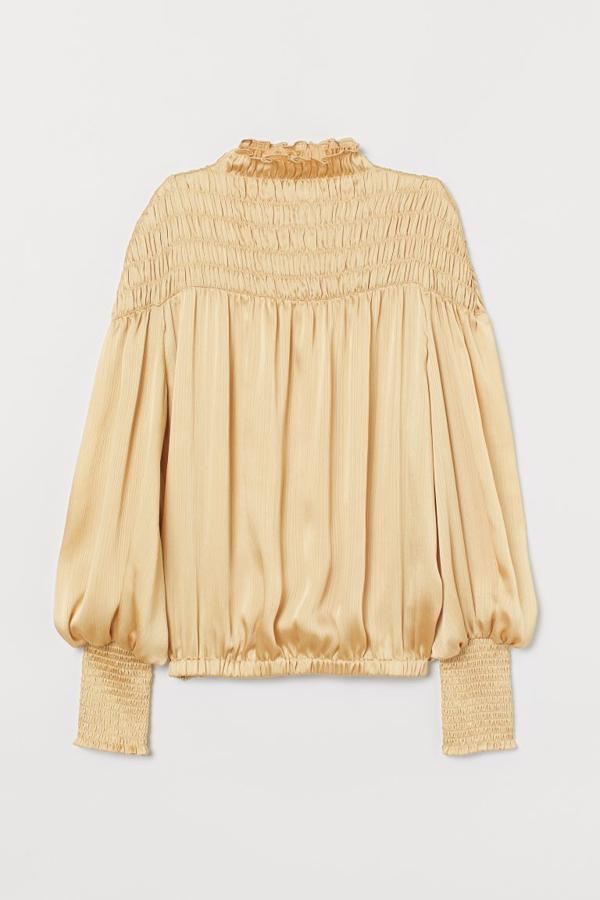 De venta exclusiva en la web de H&M es esta blusa de manga larga en tejido arrugado con brillo en color vainilla. Con cuello elevado corto con ribete de volantes y canesú fruncido, viene con los hombros marcadamente caídos y tiene un precio de 34,99 euros. Está disponible entre las tallas 32 y 46 y también en rosa empolvado.