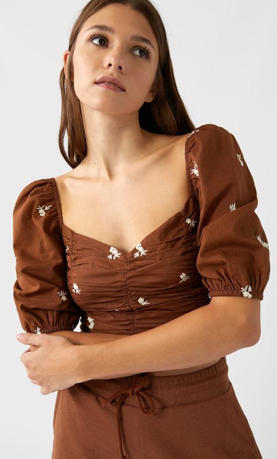 Con escote corazón y manga tres cuartos, este top fruncido en marrón chocolate es de Stradivarius y viene con detalles bordados a contraste en color blanco. Tiene un precio de 19.99 euros y está disponible en las tallas XS, S y M.
