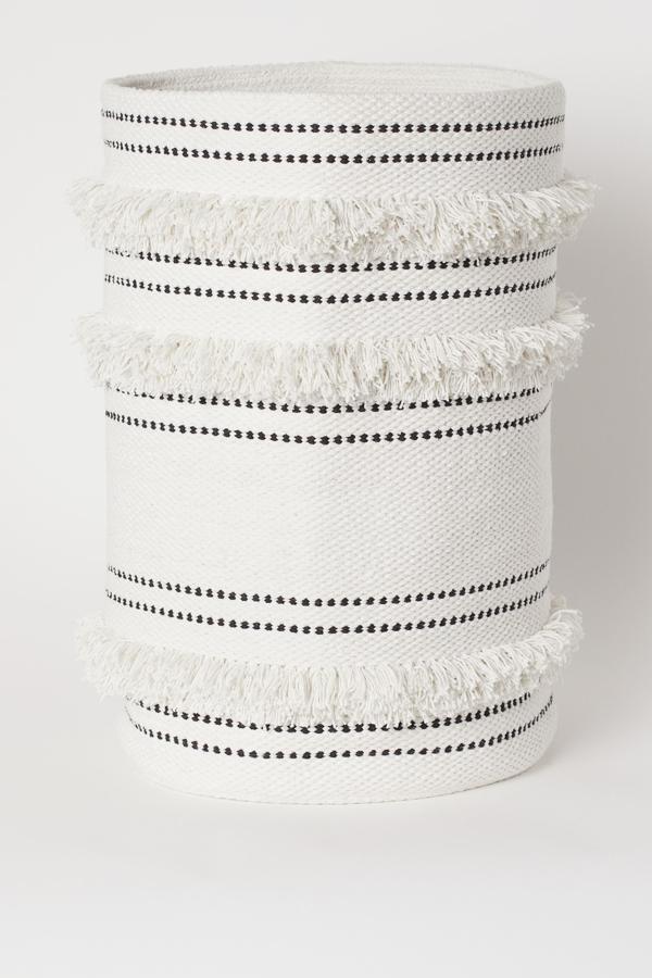 En blanco y negro, esta cesta para la colada en tejido grueso de algodón con ribete de flecos cuenta con un diámetro de 34 centímetros y una altura de 53. Tiene un precio de 24,99 euros.