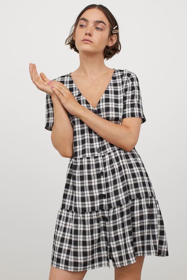 Confeccionado en viscosa y con escote de pico, este vestido corto de H&M con botones en el frontal y manga corta viene con falda evasé con fruncido escalonado. Disponible entre las tallas 32 y 44, tiene un precio de 14,99 euros.