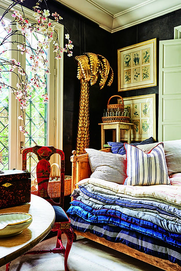 Day bed francesa de roble, cubierta con una rica colección de edredones africanos. Es una de las piezas favoritas de la decoradora: la coloca en patios, porches, bibliotecas, vestidores... para dividir el espacio. La palmera de latón forma parte de una pareja y está hecha como en los años 60.