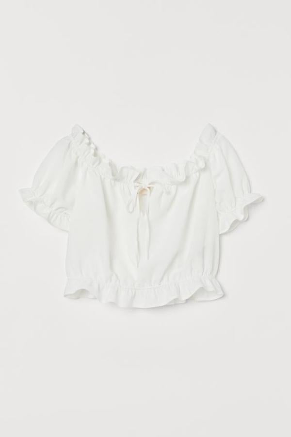En mezcla de lyocell con lino en la trama, esta blusa corta con volantes y hombros al aire de H&M viene con abertura superior con tiras de anudar y mangas cortas abullonadas. Con volante en la parte superior, mangas y bajo, tiene un precio de 29,99 euros y está disponible entre las tallas 42 y 50.