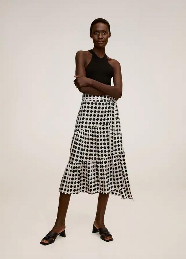 Diseño acampanado con cinturón ajustable a tono para esta falda en color crudo con estampado de lunares negros con bajo asimétrico. Es de Mango, cuesta 49,99 euros y está disponible entre las tallas XS y XL.