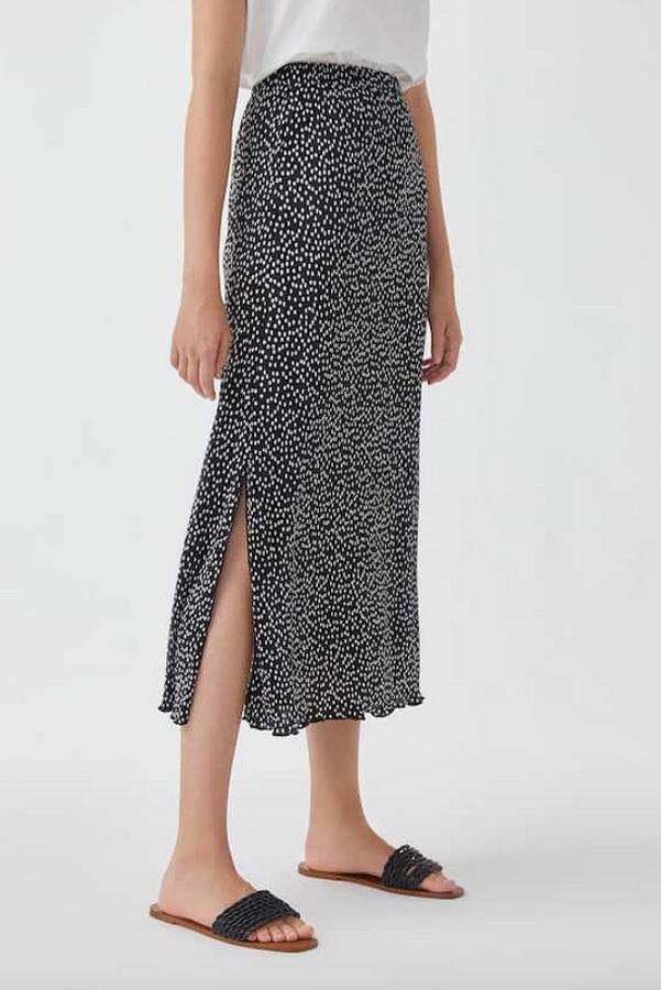 Tejido plisado mini con estampado de manchas blancas sobre fondo negro para esta falda midi de Pull&Bear con aberturas laterales. Tiene un precio de 17,99 euros y está disponible entre las tallas XS y L.