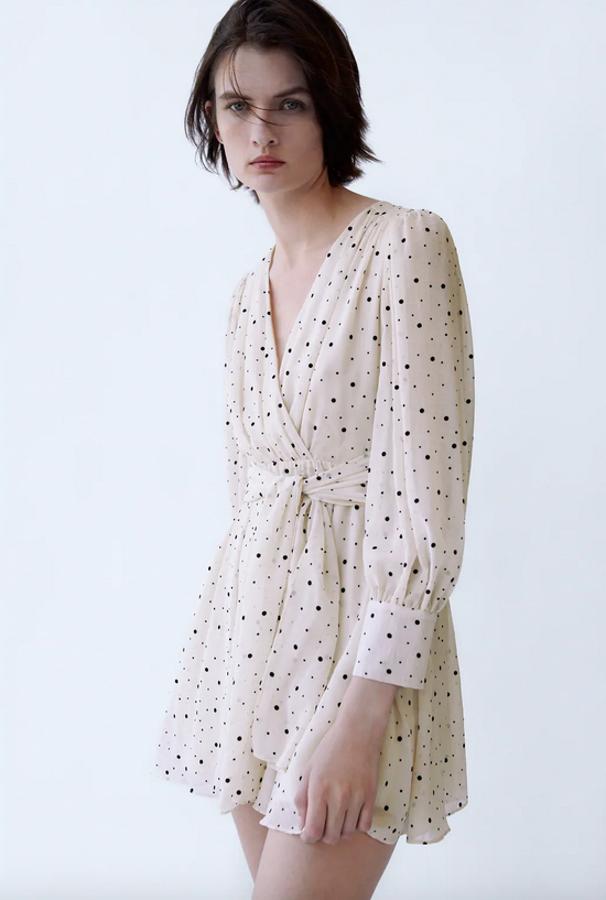 Escote de pico cruzado y manga larga para este vestido corto de Zara en color crudo con estampado de minilunares. Con detalle de lazo delantero, cuesta 39,95 euros y está disponible entre las tallas XS y XL.
