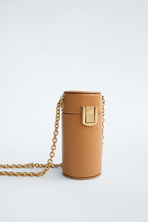 Este mini bolso con forma cilíndrica en color tostado cuenta con cierre con broche y asa metálica en el hombro. Con detalle de espejo en el interior, es de Zara y tiene un precio de 12,95 euros.