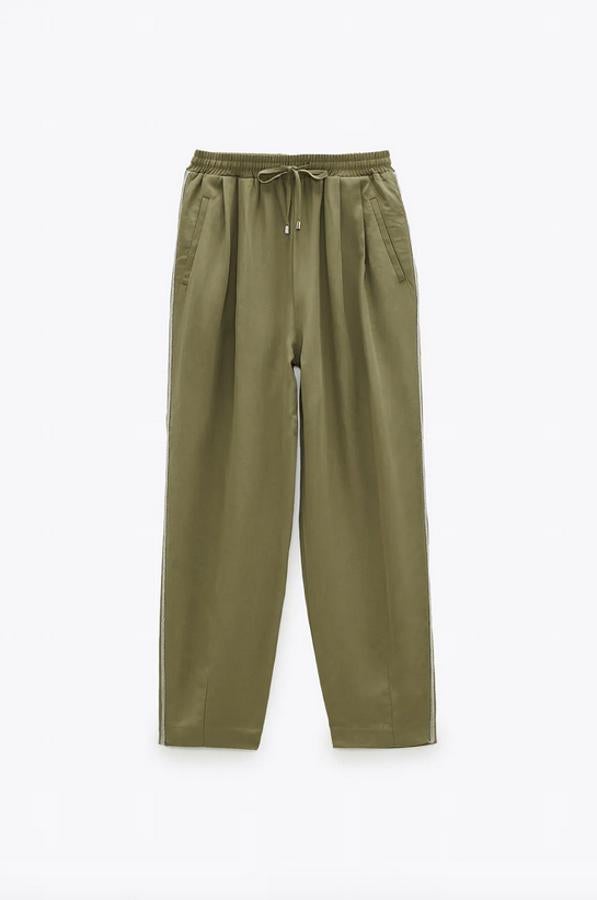 Este pantalón de tiro alto con cintura elástica ajustable con cordones en color caqui es de Zara y viene con banda lateral combinada a contraste con aplicación de abalorios. Tiene un precio de 25,95 euros y está disponible entre las tallas XS y XL.