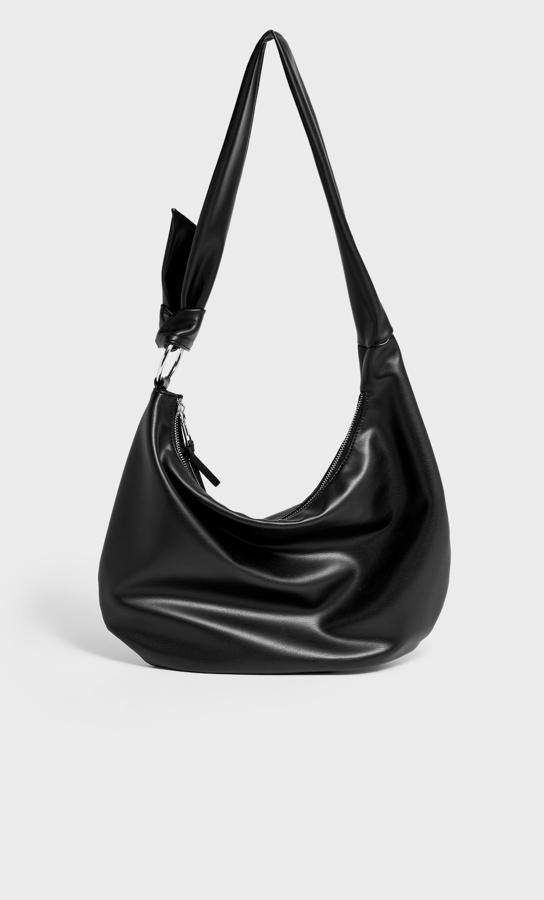 Con anilla metalizada que une el bolso con el asa con un nudo, esta bandolera de Stradivarius es ideal para las amantes de los bolsos grandes. En color negro, cuesta 19,99 euros.