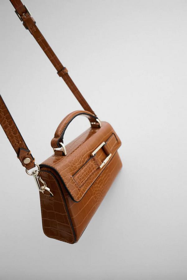 Disponible en naranja teja o en negro, esta bandolera con asa de mano tiene el cuerpo rígido con detalle metalizado en la solapa. Es de Zara y cuesta 19,95 euros.