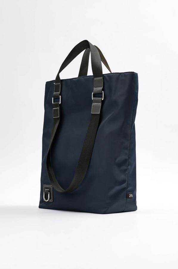 En azul marino con corte de nylon, este bolso en formato shopper de Zara viene con detalle de mosquetón metálico en la parte delantera, asas de mano y de hombro en contraste y compartimento principal con colgador y dos bolsillos. Pertenece a la colección sostenible de la firma y cuesta 39,95 euros.