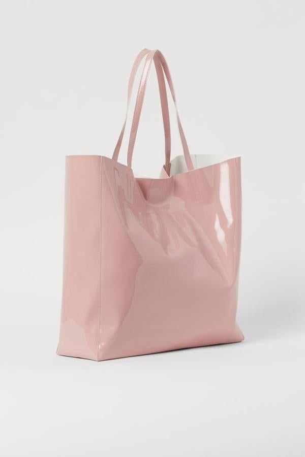 En piel sintética con dos asas y cierre magnético oculto arriba, este bolso shopper de H&M en rosa claro viene con acabado acharolado. Cuesta 19,99 euros, solo podemos comprarlo en la web de la firma y está disponible también en gris oscuro y en negro.