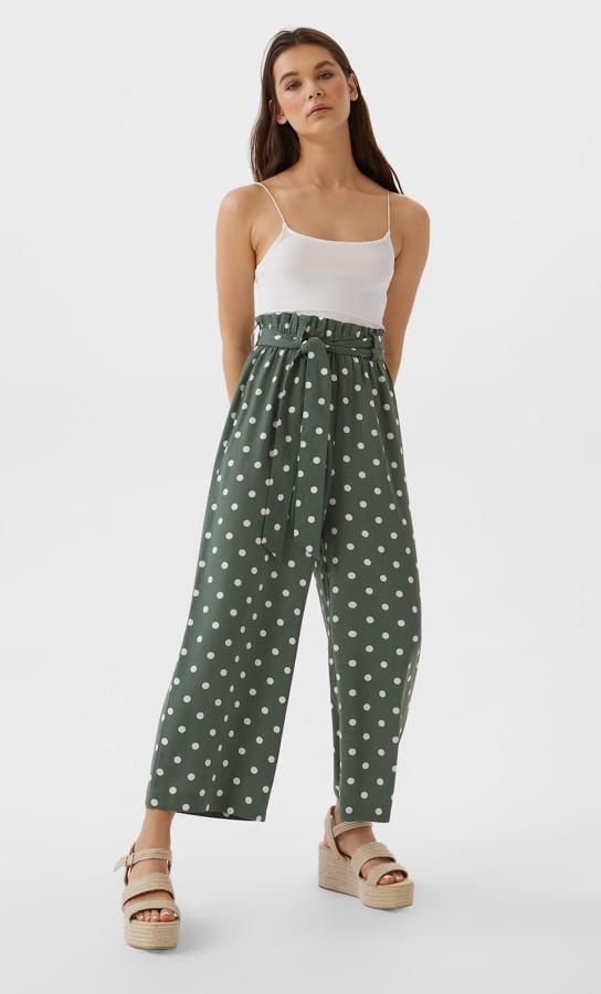 En color verde con topos blancos, este pantalón de tiro alto con cintura elástica cuenta con trabillas y pinzas en la parte delantera. Cuenta con cinturón del mismo tejido y tiene un precio de 11,19 euros.