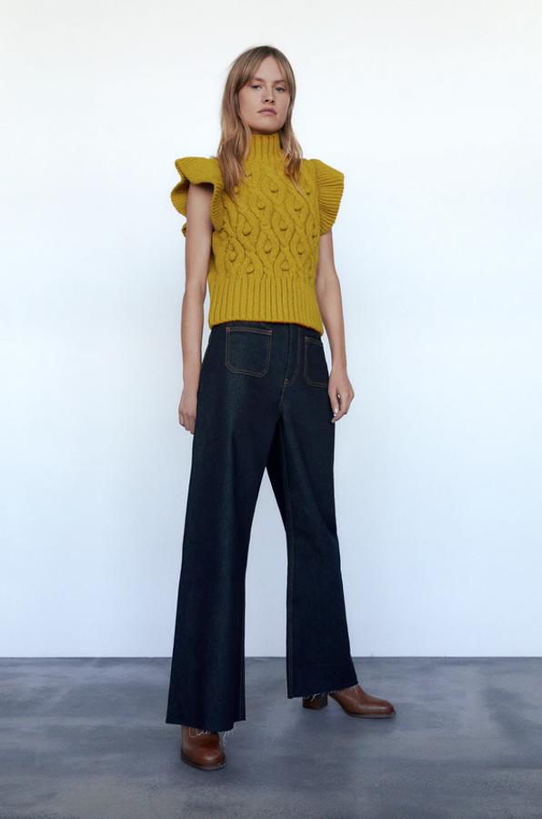 En color oliva, con volantes en los hombros, cuello subido y pompones en el diseño trenzado, este chaleco de punto de Zara cuesta 25,95 euros y está disponible en las tallas S, M y L.