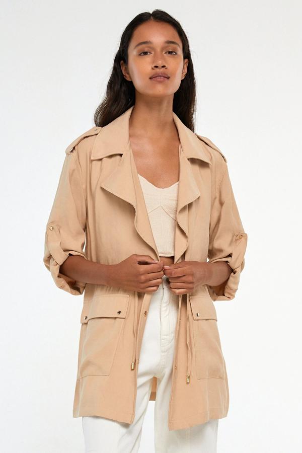 Esta cazadora de estilo sahariana con detalle de cordón ajustable a la cintura cuenta con cuello solapa, bolsillos laterales y cierre mediante botones. Disponible en color ocre o arena, tiene un precio de 19,99 euros.