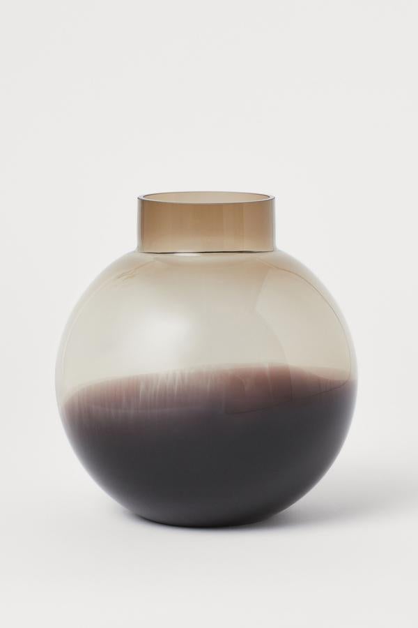 En color beige, este jarrón redondo de vidrio con base tonalizada tiene una altura de 21 centímetros y un diámetro de 20. Cuesta 17,99 euros.