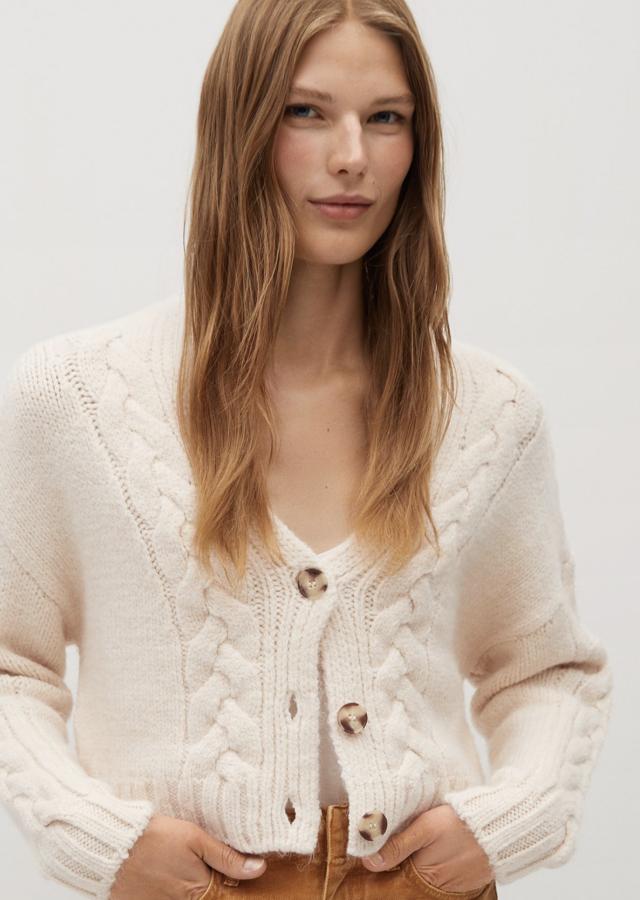 Este cárdigan de punto en tejido de ochos está disponible en crudo o en rojo. Con cuello de pico y cierre de botones de efecto carey, es de Mango y tiene un precio de 29,99 euros.