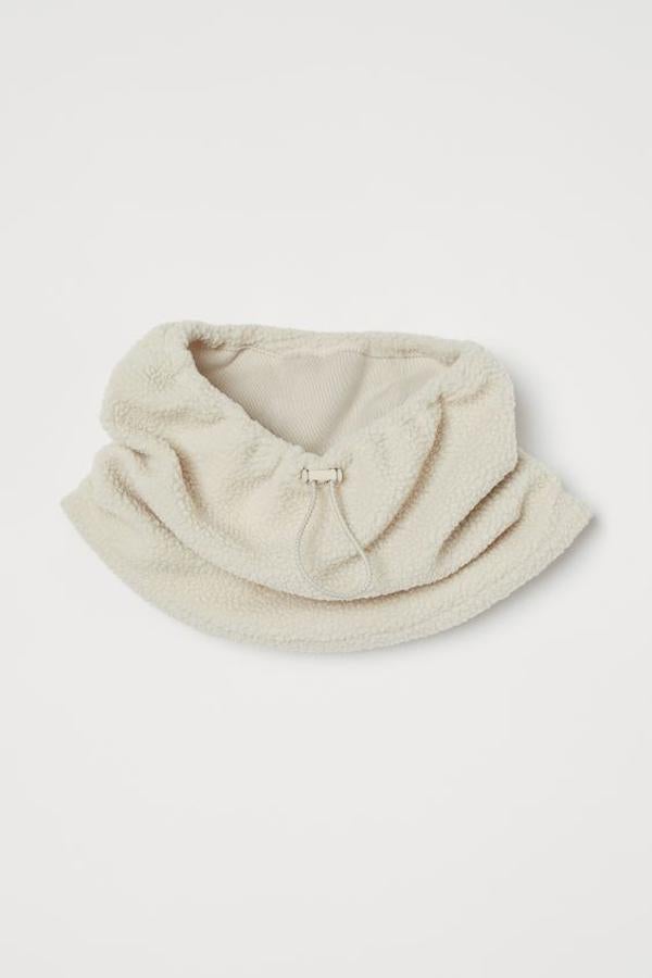 En polar cálido suave con cordón de ajuste y color beige, esta bufanda de tubo con bajo asimétrico está confeccionada en poliéster parcialmente reciclado y tiene un precio de 9,99 euros.
