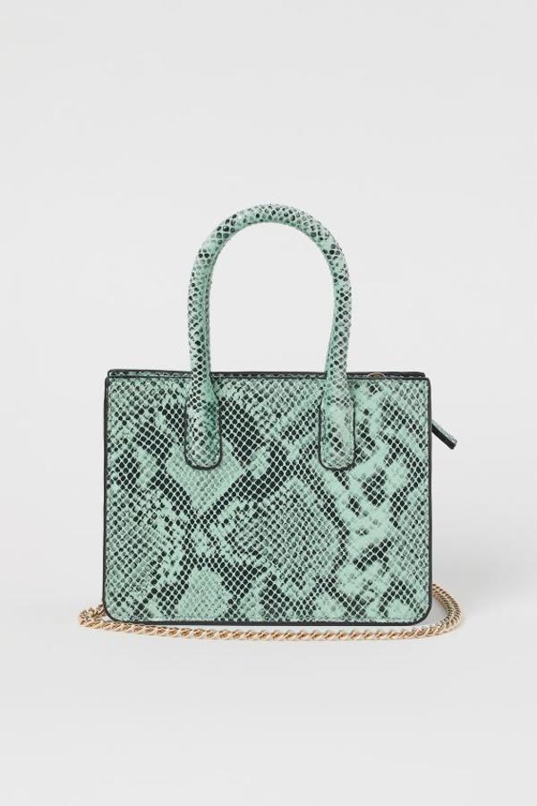 Este bolso rígido mini de H&M está confeccionado en piel sintética y viene con dos asas cortas y cierre de cremallera, y una cadena de metal extraíble en dorado. Tiene un precio de 24,99 euros.