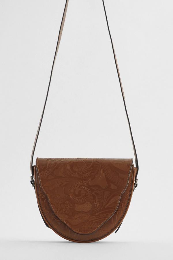En color marrón, este bolso bandolera de piel con cuerpo con detalle de grabados y bolsillo en la parte delantera y trasera cuenta con asa de hombro ajustable e interior borrado. Es de Zara y tiene un precio de 49,95 euros.